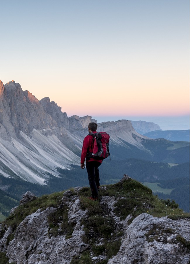 The picture shows a walking man resting at a vantage point and admiring the Dolomites in the sunset.
