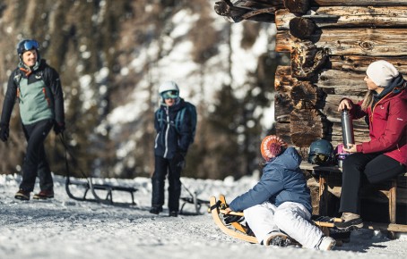 The picture shows a family having fun tobogganing in Villnöss.