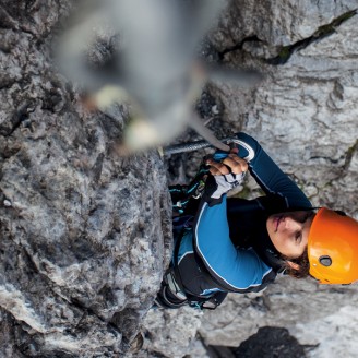 The picture shows a woman from above, who is pulling herself upwards on a steel rope. She is in the middle of a demanding via ferrata.