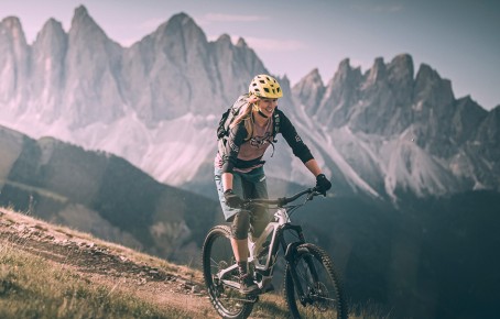 The picture shows a woman enjoying the downhill ride. In the background the Geisler Dolomites
