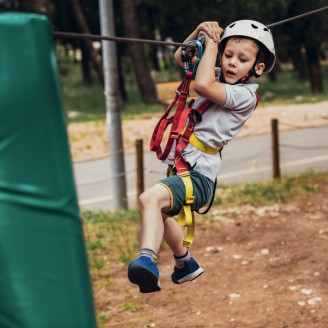 The picture shows a little boy hanging from the ropeway in the high ropes course in Villnöss.