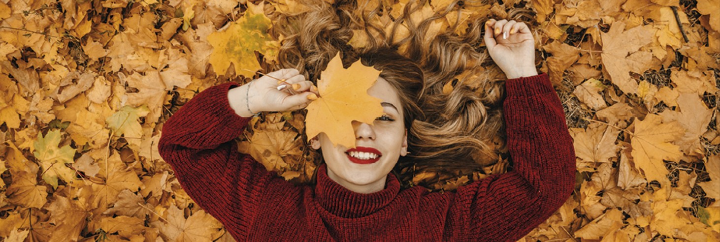 teiser stern Villnöss Eisack Valley South Tyrol – Autumn vacation The picture shows a woman lying among the autumn leaves and holding one to her face. She is smiling.